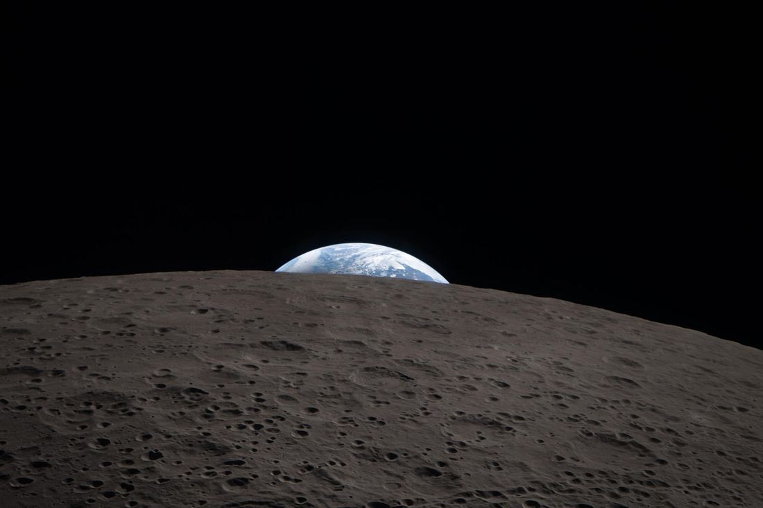 Earth as a small crescent setting behind the curved horizon of the Moon