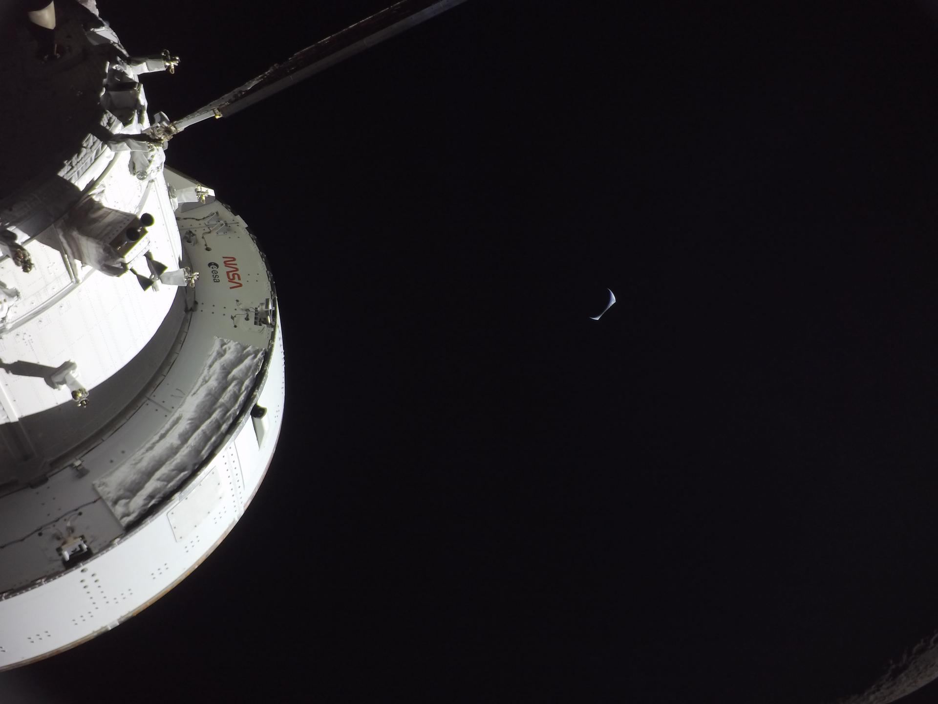 A thin crescent Earth rising beyond the gray, cratered limb of the Moon, seen from the Orion spacecraft