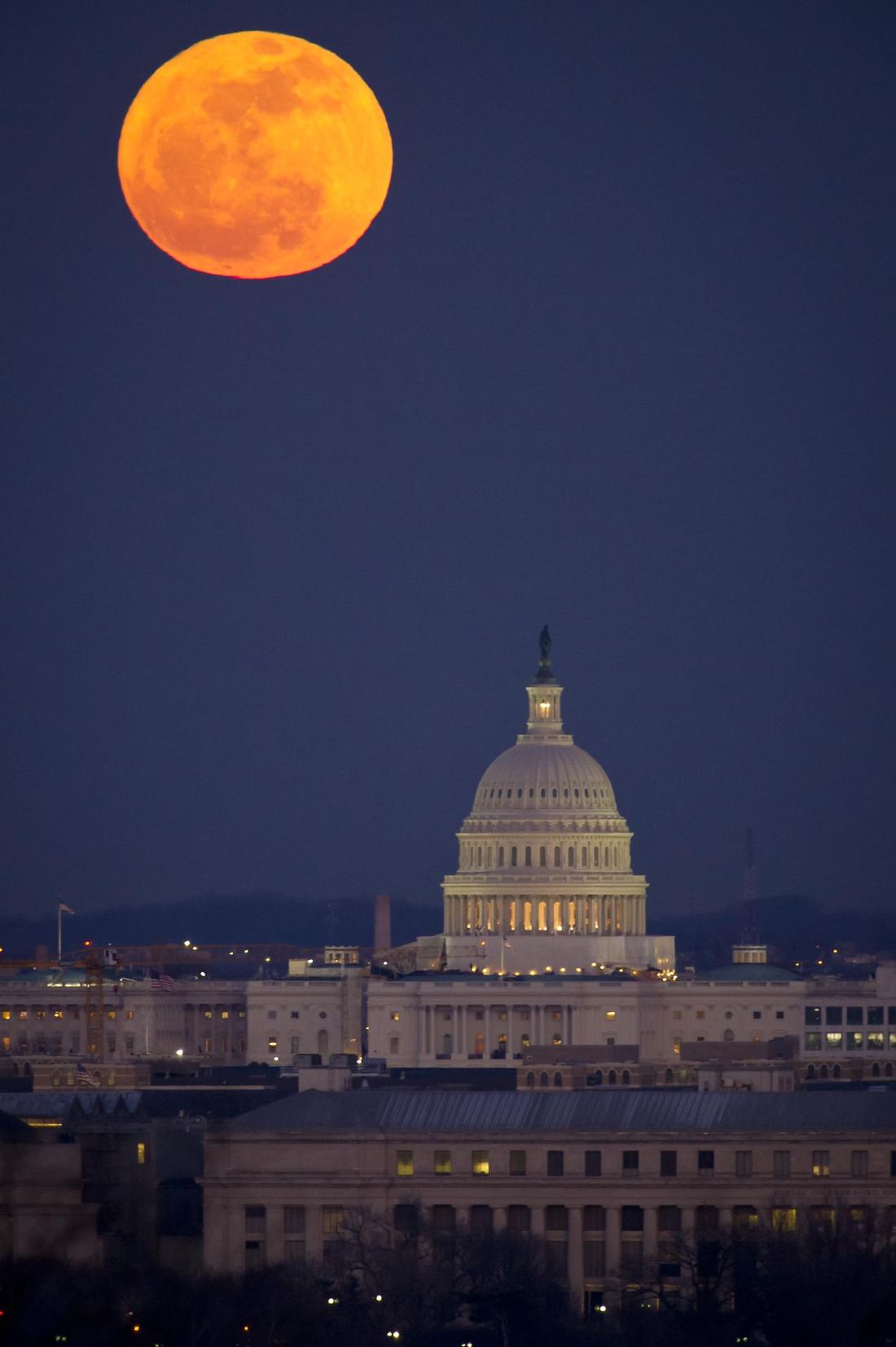 A bright full Moon rising in a deep blue evening sky above the dome of the U.S. Capitol